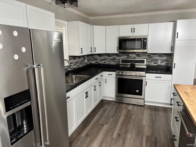 kitchen with white cabinets, wooden counters, stainless steel appliances, decorative backsplash, and sink