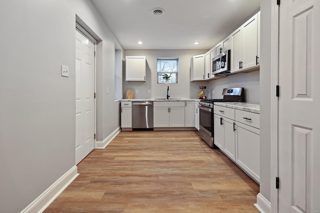 kitchen featuring white cabinetry, appliances with stainless steel finishes, sink, and light wood-type flooring