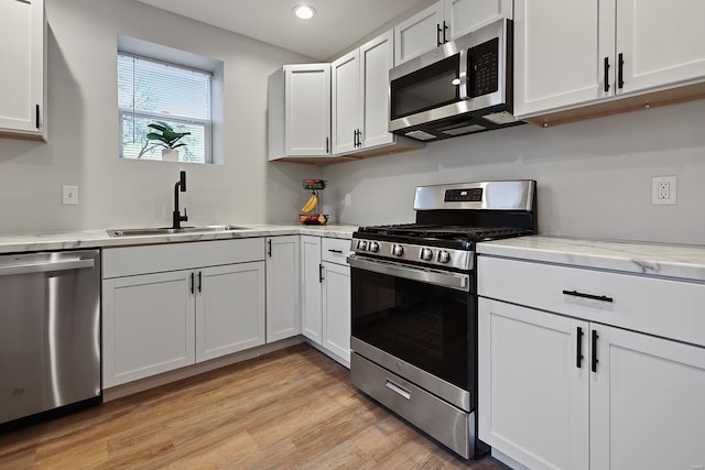 kitchen with sink, white cabinets, stainless steel appliances, light stone countertops, and light wood-type flooring