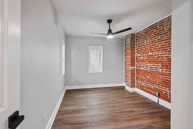 spare room with dark wood-type flooring, ceiling fan, and brick wall