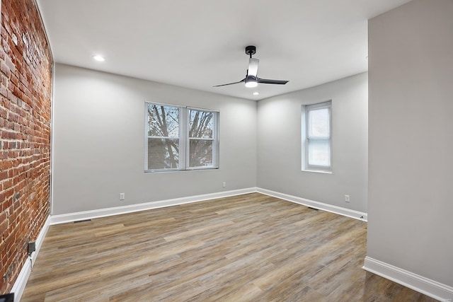 spare room featuring ceiling fan, brick wall, and light wood-type flooring