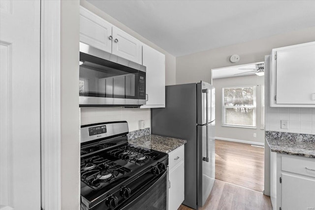 kitchen featuring light wood-type flooring, dark stone counters, white cabinets, and appliances with stainless steel finishes