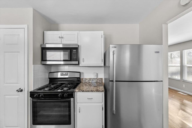 kitchen with stainless steel appliances, wood-type flooring, white cabinets, decorative backsplash, and dark stone counters