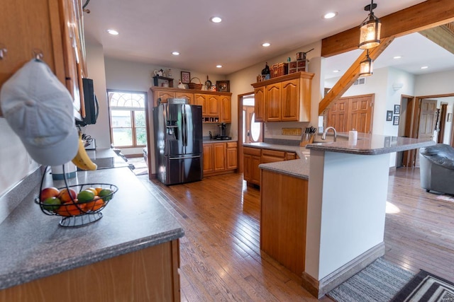 kitchen with light hardwood / wood-style floors, a kitchen breakfast bar, kitchen peninsula, black fridge with ice dispenser, and beam ceiling