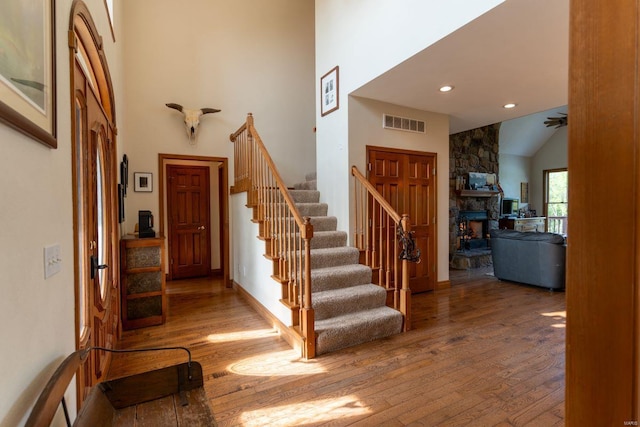 foyer with ceiling fan, lofted ceiling, hardwood / wood-style flooring, and a stone fireplace