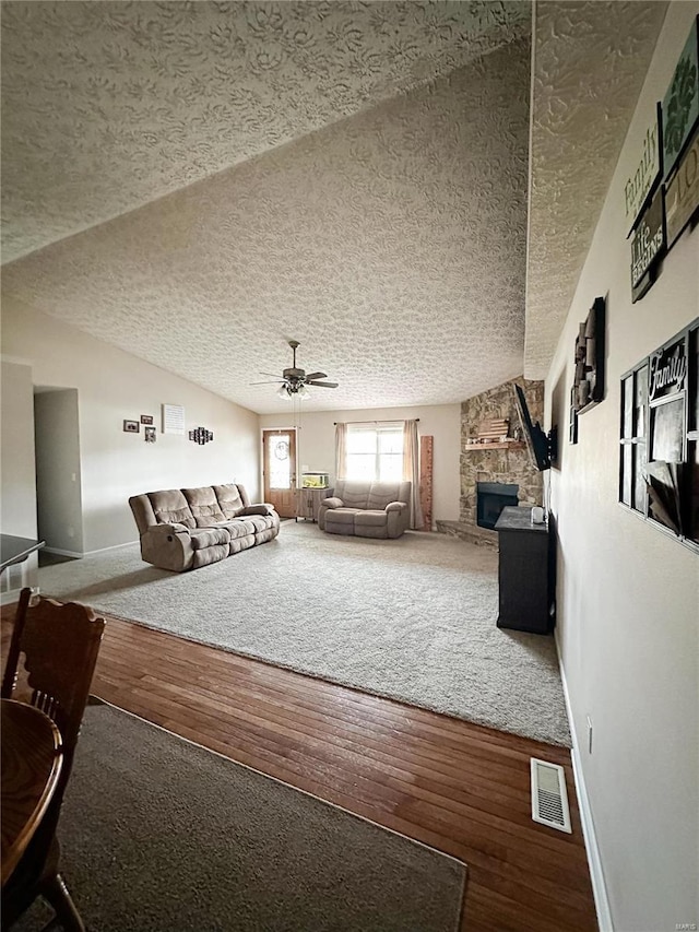 unfurnished living room with ceiling fan, hardwood / wood-style flooring, a textured ceiling, and a stone fireplace