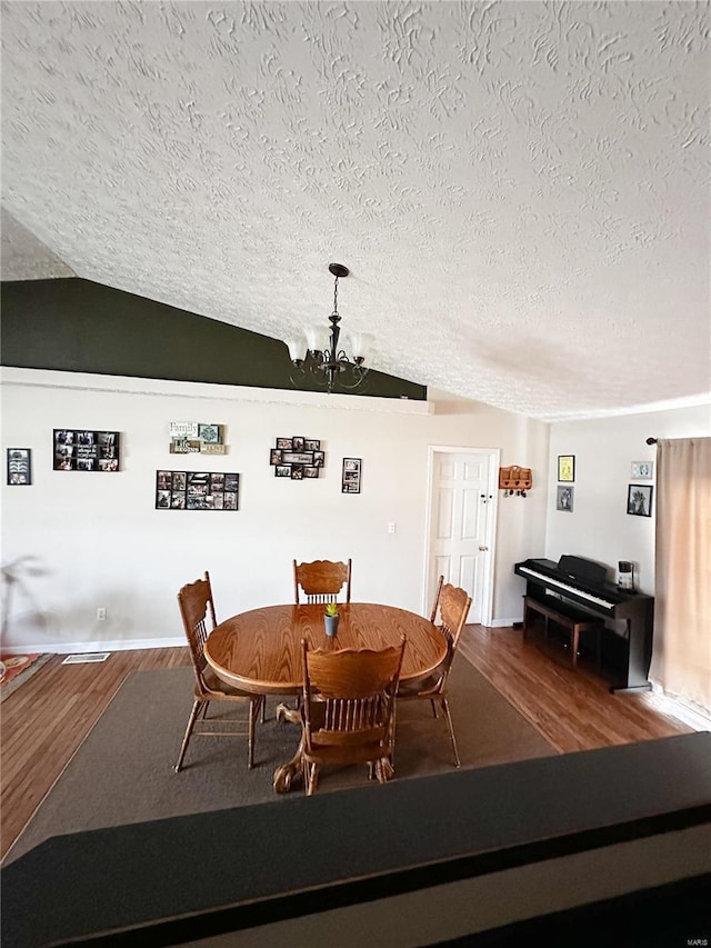 dining room with hardwood / wood-style flooring, a textured ceiling, a chandelier, and vaulted ceiling