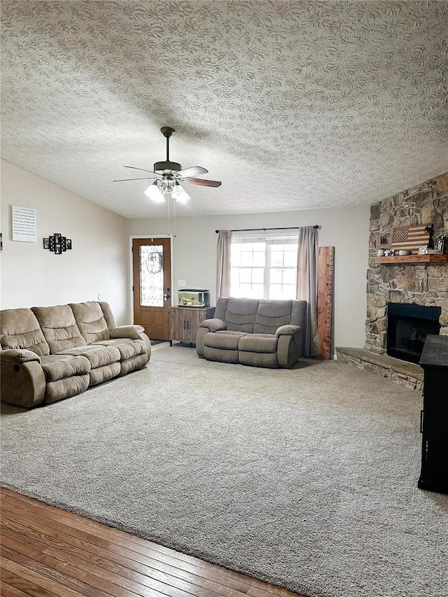 living room featuring ceiling fan, a textured ceiling, hardwood / wood-style flooring, and a fireplace