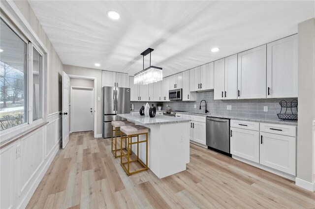 kitchen featuring a kitchen island, appliances with stainless steel finishes, decorative light fixtures, white cabinets, and light stone countertops