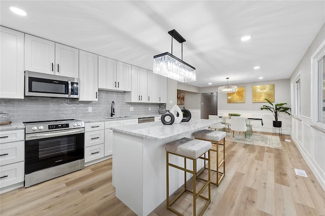 kitchen with appliances with stainless steel finishes, white cabinetry, sink, hanging light fixtures, and light stone counters