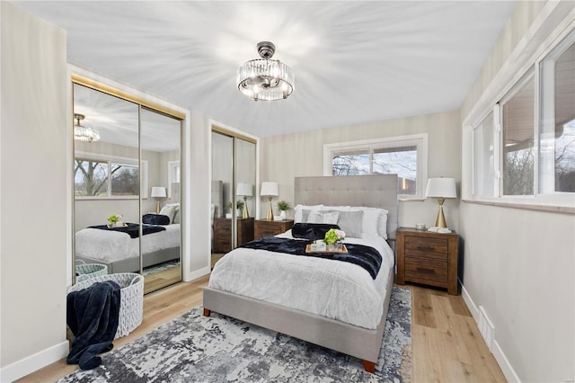 bedroom featuring a chandelier, light wood-type flooring, multiple windows, and two closets