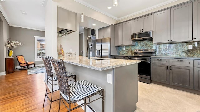 kitchen with a breakfast bar, light stone countertops, appliances with stainless steel finishes, gray cabinetry, and ornamental molding