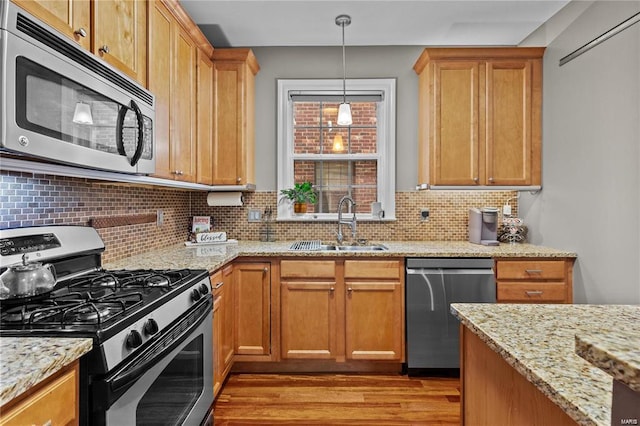 kitchen with appliances with stainless steel finishes, decorative backsplash, light hardwood / wood-style flooring, light stone counters, and sink