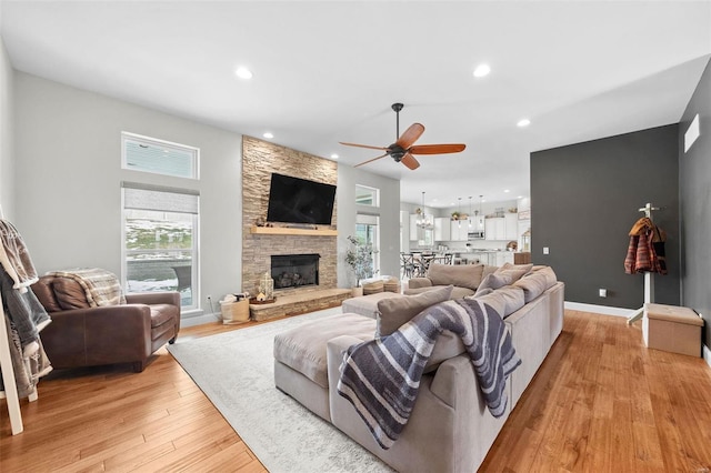 living room featuring ceiling fan, a stone fireplace, and light hardwood / wood-style floors