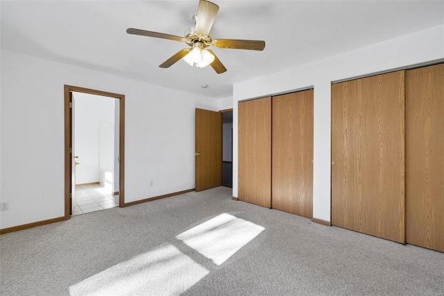 unfurnished bedroom with light colored carpet, two closets, and ceiling fan