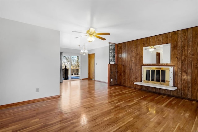 unfurnished living room featuring wood-type flooring, ceiling fan with notable chandelier, and wood walls