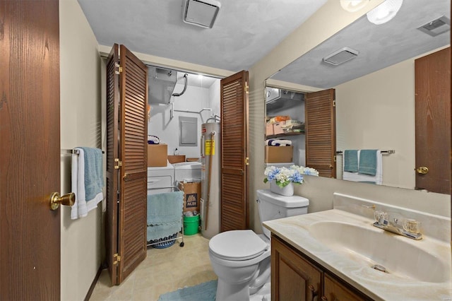 bathroom featuring vanity, toilet, washing machine and dryer, and electric water heater