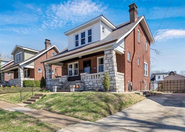 view of front of house with stone siding, a front lawn, covered porch, and brick siding