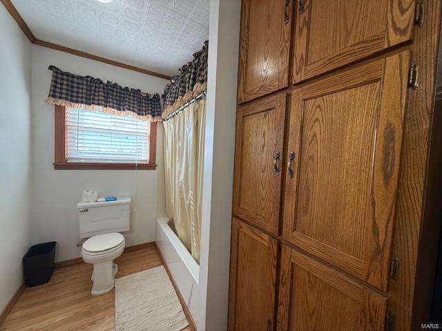 bathroom featuring toilet, hardwood / wood-style floors, shower / tub combo with curtain, and crown molding