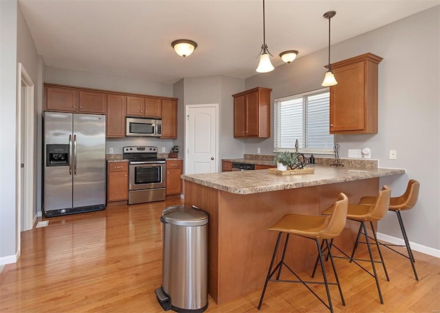 kitchen with appliances with stainless steel finishes, decorative light fixtures, kitchen peninsula, light wood-type flooring, and a breakfast bar area