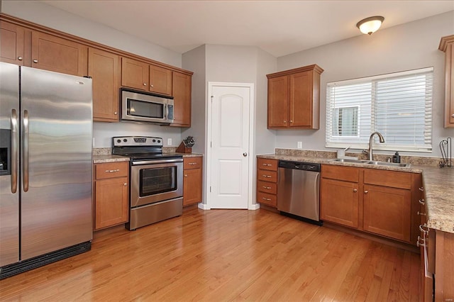 kitchen with sink, light wood-type flooring, light stone countertops, and stainless steel appliances