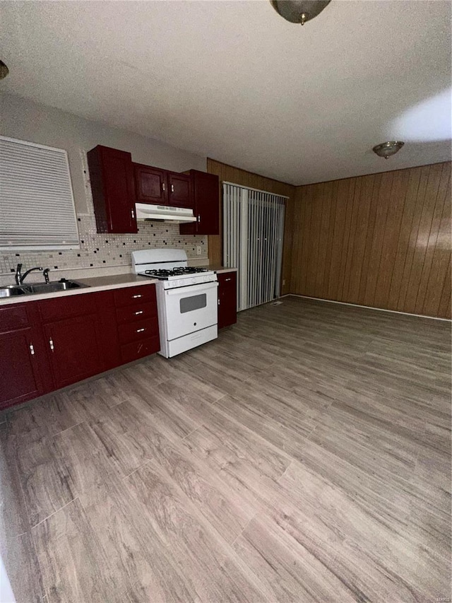 kitchen featuring sink, wood walls, a textured ceiling, light wood-type flooring, and white gas range