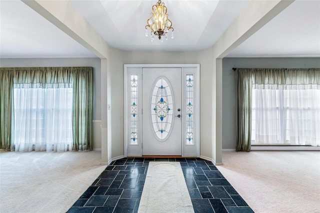 foyer entrance with an inviting chandelier, a wealth of natural light, and dark colored carpet