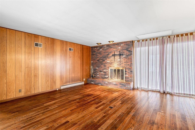 unfurnished living room with a brick fireplace, dark hardwood / wood-style floors, baseboard heating, and wood walls