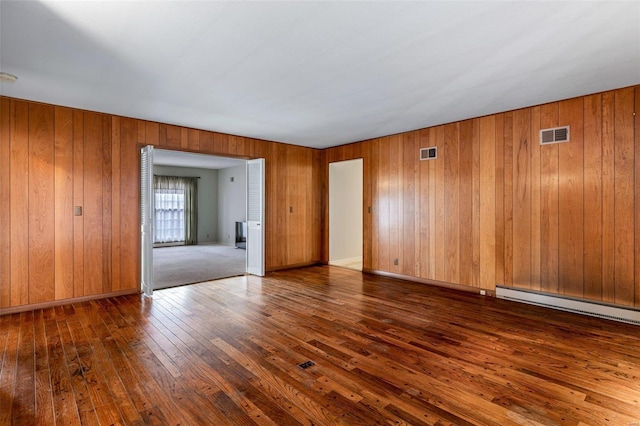 empty room with a baseboard radiator, dark hardwood / wood-style floors, and wood walls