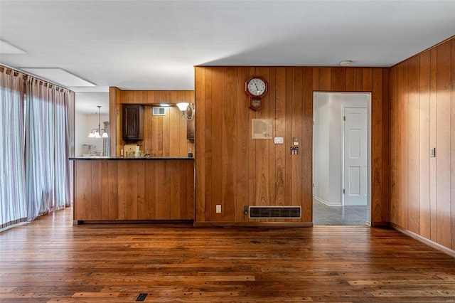 interior space with dark wood-type flooring, wooden walls, and an inviting chandelier