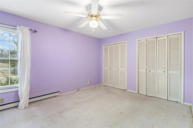 unfurnished bedroom featuring ceiling fan, a baseboard heating unit, light colored carpet, and two closets