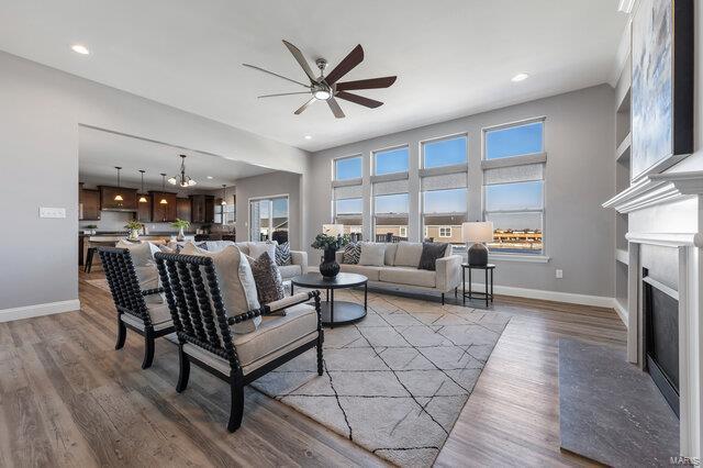 living room featuring hardwood / wood-style flooring, ceiling fan with notable chandelier, and a fireplace