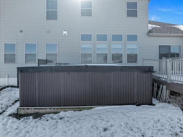 snow covered back of property featuring a wooden deck and a jacuzzi