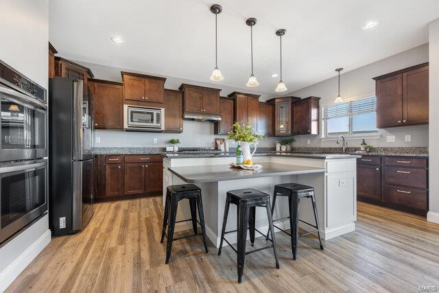 kitchen with a kitchen island, pendant lighting, a breakfast bar area, light hardwood / wood-style floors, and stainless steel appliances