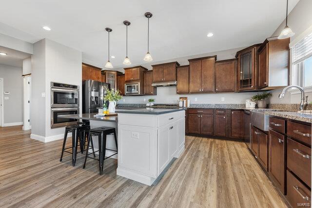 kitchen featuring a kitchen island, pendant lighting, a breakfast bar area, stainless steel appliances, and light hardwood / wood-style flooring