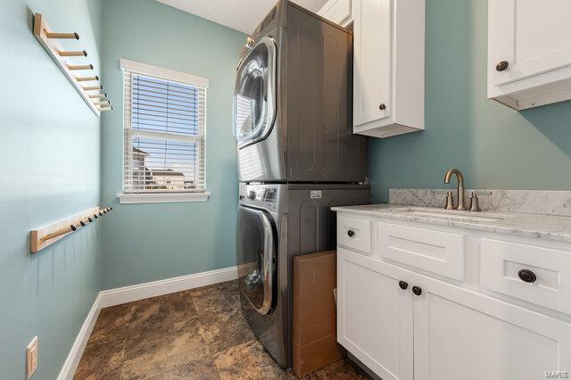 washroom with cabinets, stacked washer / dryer, and sink