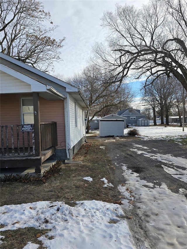 view of snow covered exterior featuring a porch and a storage unit