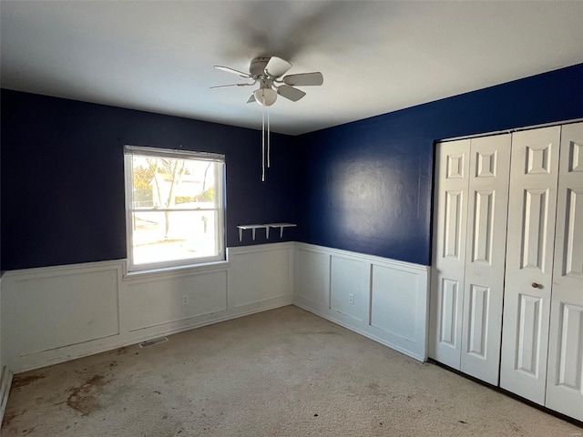 unfurnished bedroom with visible vents, a wainscoted wall, carpet floors, ceiling fan, and a closet