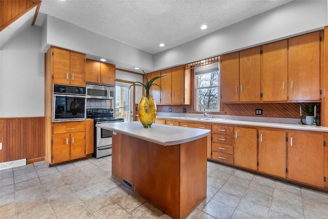 kitchen with sink, a center island, a textured ceiling, appliances with stainless steel finishes, and wooden walls