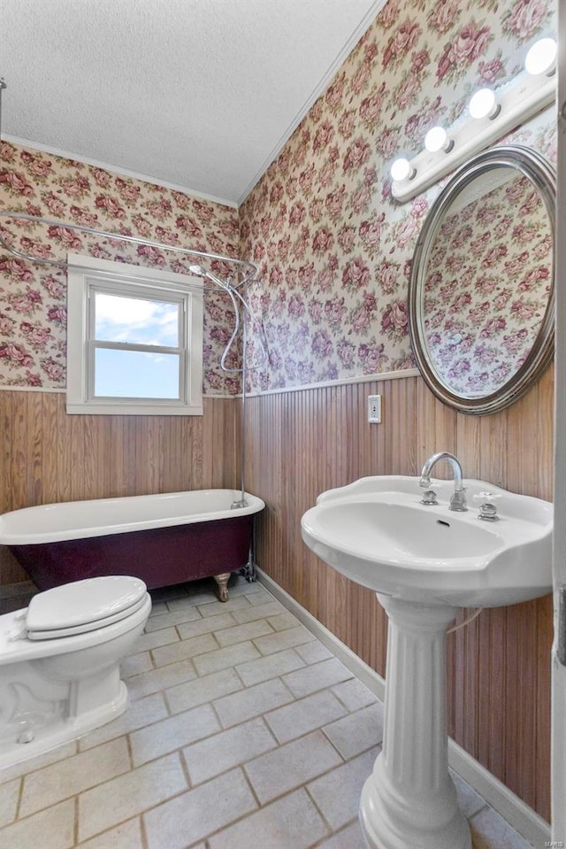 bathroom featuring a tub to relax in, toilet, sink, a textured ceiling, and ornamental molding