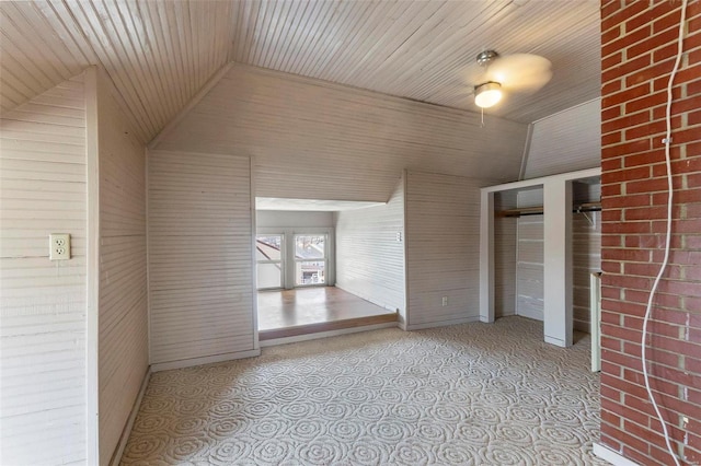 empty room featuring vaulted ceiling, wooden ceiling, and wooden walls