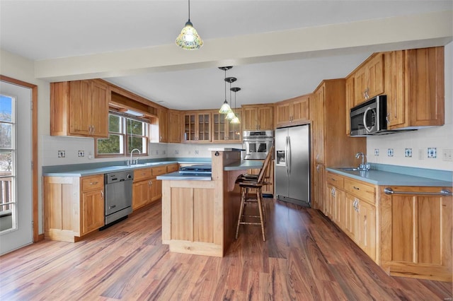 kitchen with a kitchen bar, appliances with stainless steel finishes, wood-type flooring, sink, and a kitchen island