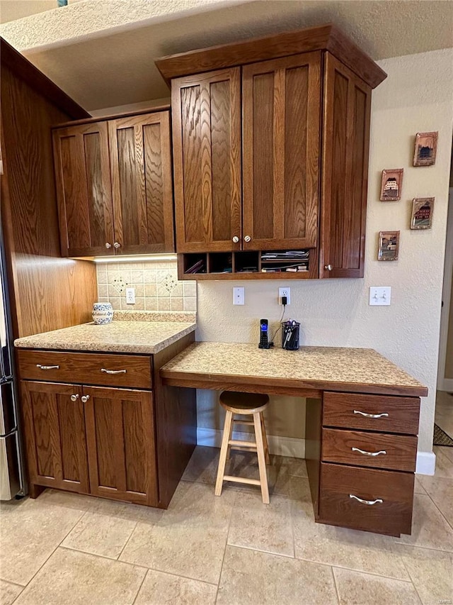 kitchen featuring a kitchen bar, built in desk, a textured ceiling, and light tile patterned floors