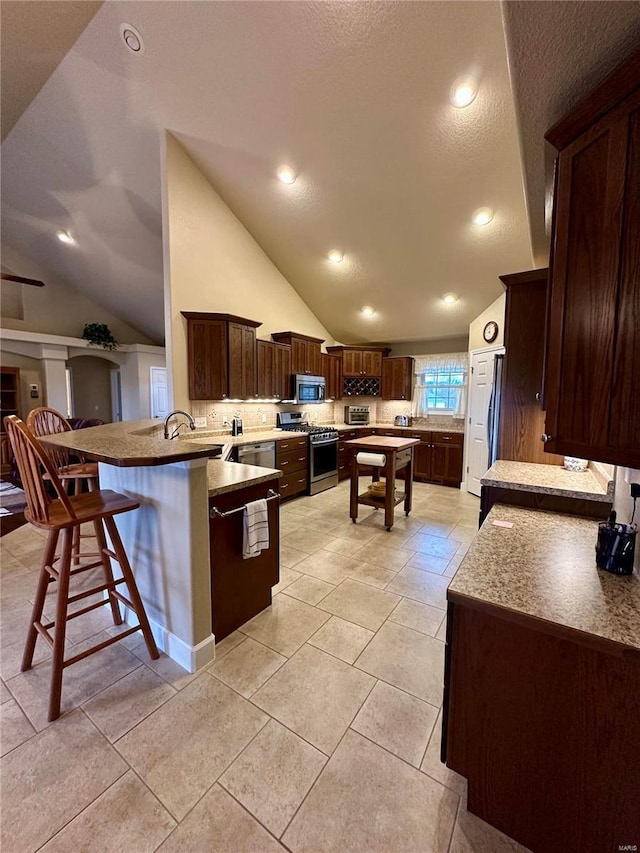 kitchen featuring stainless steel appliances, lofted ceiling, a kitchen breakfast bar, and kitchen peninsula