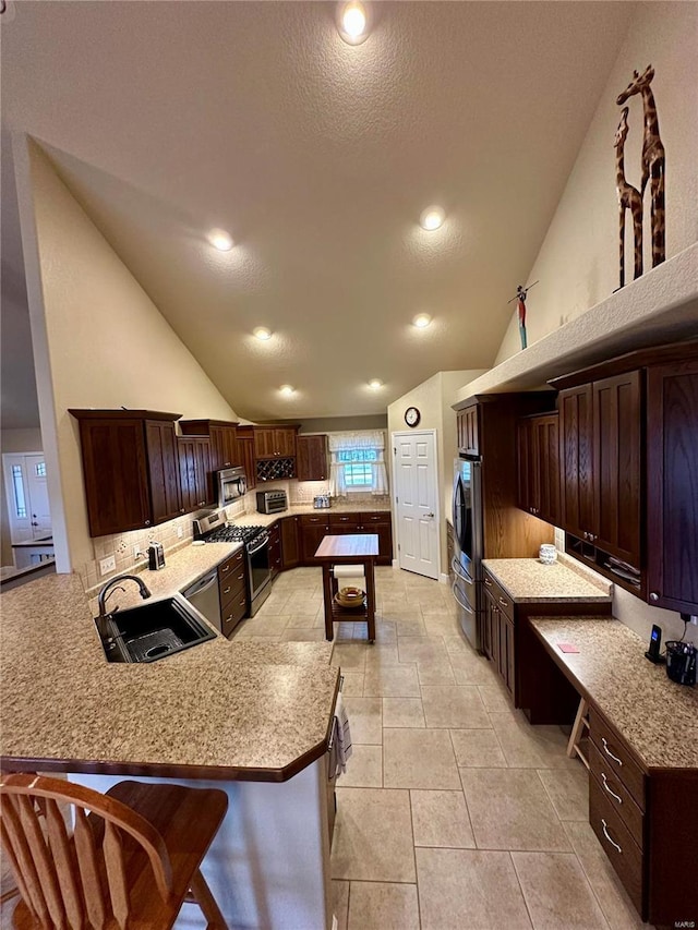 kitchen with sink, light tile patterned floors, appliances with stainless steel finishes, a kitchen breakfast bar, and kitchen peninsula