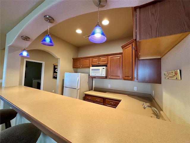 kitchen with white appliances, decorative light fixtures, kitchen peninsula, and a breakfast bar area