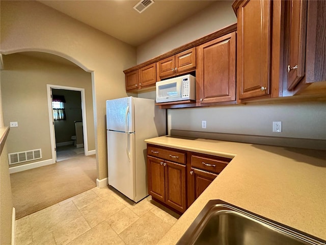 kitchen featuring white appliances, sink, and light carpet