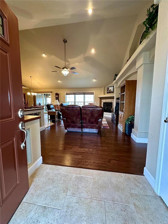 living room with hardwood / wood-style floors, ceiling fan with notable chandelier, vaulted ceiling, and built in features