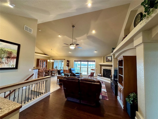 living room with a stone fireplace, dark hardwood / wood-style floors, ceiling fan with notable chandelier, and high vaulted ceiling