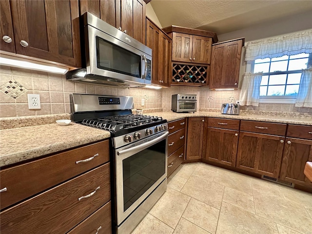 kitchen featuring stainless steel appliances, light stone countertops, decorative backsplash, and light tile patterned floors